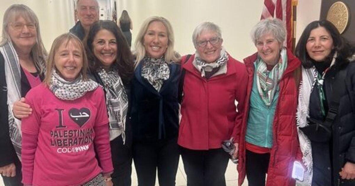 Group of activists posing in a hallway, wearing scarves and diverse outfits, with an American flag in the background, advocating for Palestinian liberation.