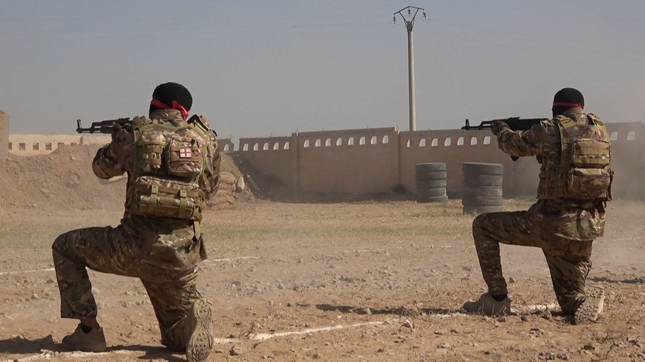 Soldiers in tactical gear practice shooting in a dusty training environment, demonstrating military readiness and teamwork.