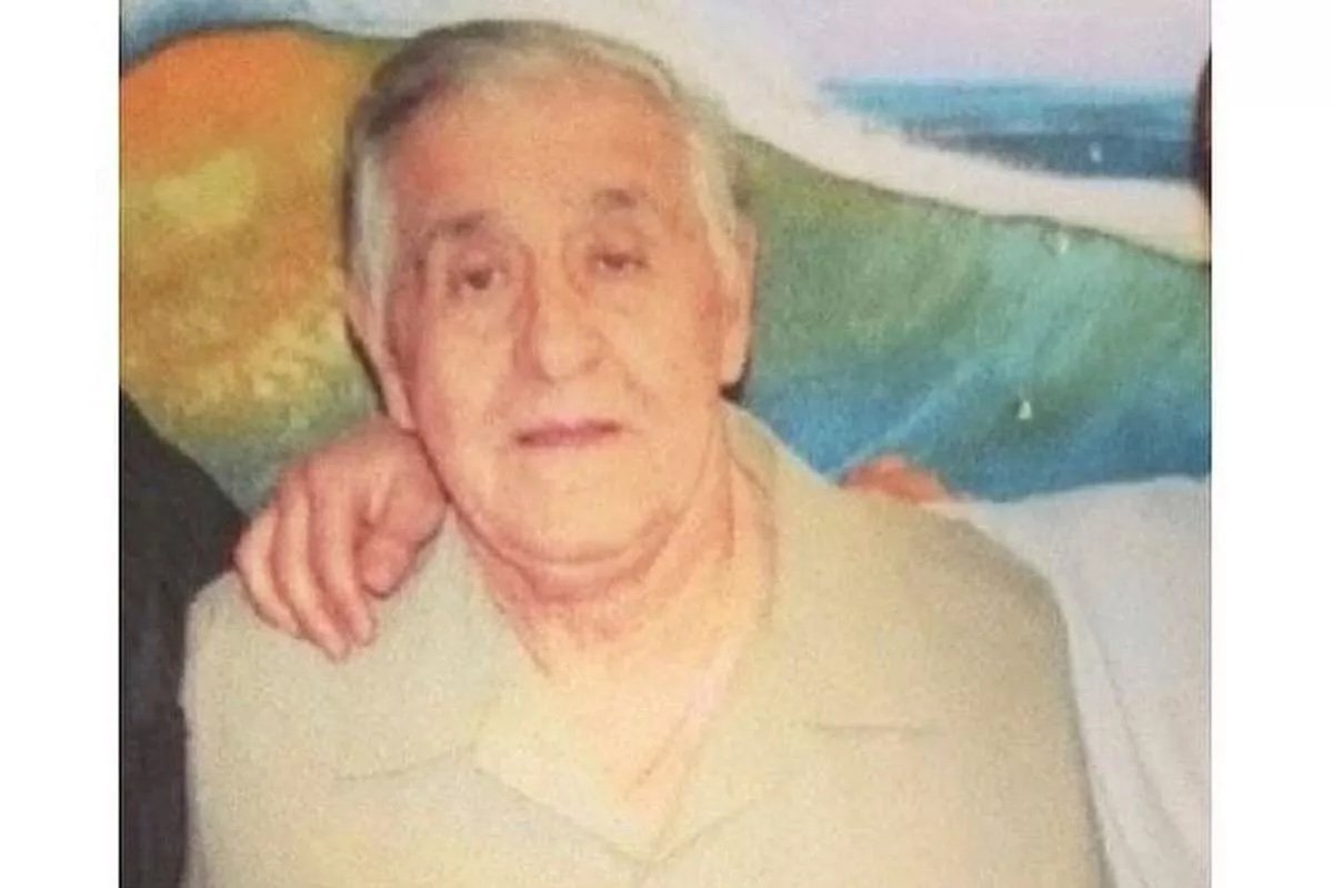 Elderly man in a beige shirt smiling, with a colorful beach scene in the background, representing warmth and nostalgia.