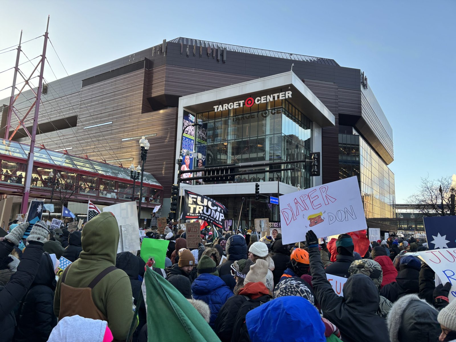 Crowd protesting outside the Target Center, holding signs with political messages during a rally.