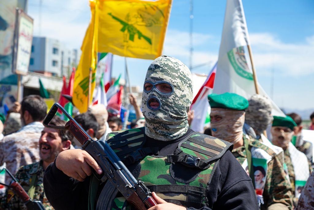 Masked individuals in military attire participate in a demonstration, holding flags and weapons, highlighting political tensions in the region.