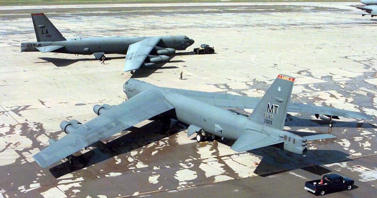 Two military aircraft, a B-52 and a cargo plane, parked on a military airfield with a service vehicle nearby.