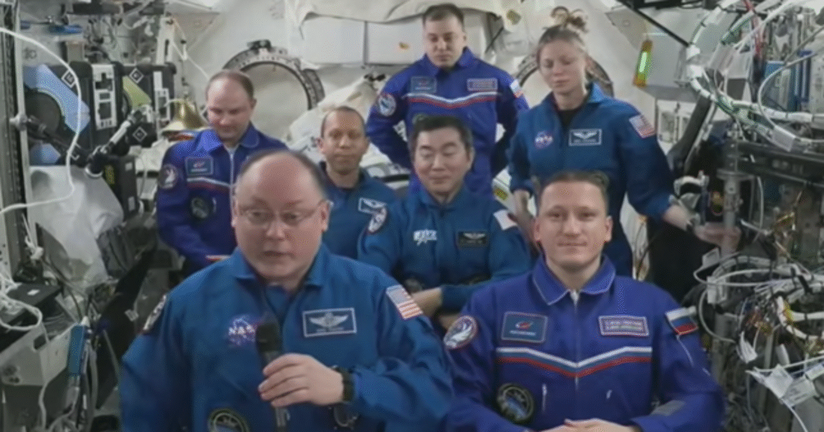 Astronauts in blue space suits participate in a video conference aboard the International Space Station, showcasing international collaboration in space exploration.