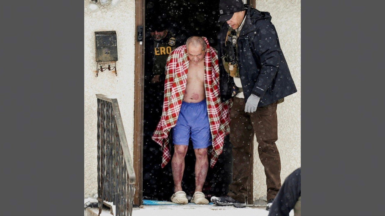 Law enforcement officials escort a shirtless man wrapped in a blanket out of a house during a snowstorm.