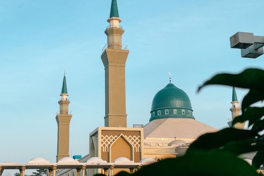 Mosque with green dome and tall minarets against a blue sky, showcasing Islamic architecture and serene ambiance.