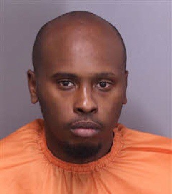 Mugshot of a man wearing an orange jumpsuit, displaying a serious expression against a gray background.