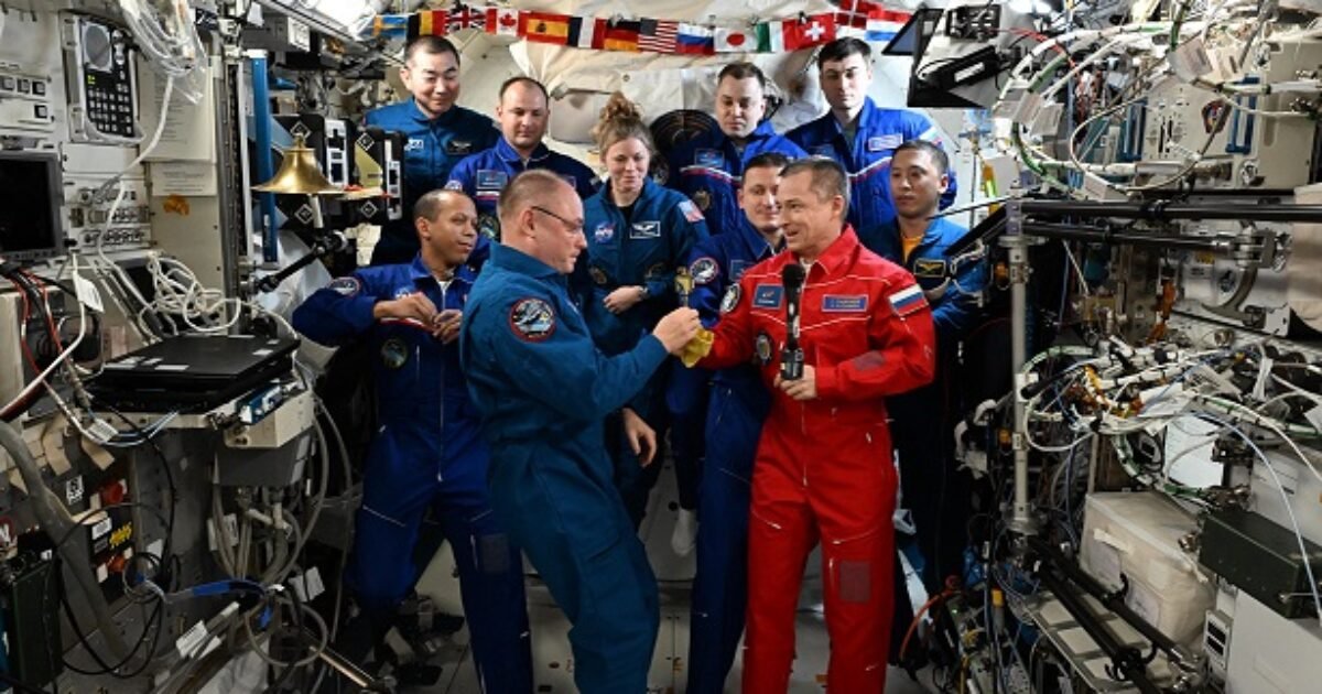 Astronauts in space aboard the International Space Station engage in a team activity, surrounded by scientific equipment and international flags.
