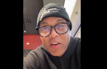 Man wearing glasses and a beanie speaks directly to the camera in a casual restaurant setting.