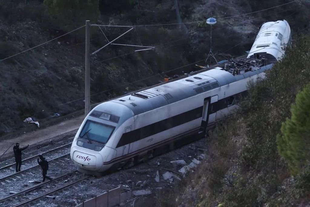 Derailed Renfe train on tracks with emergency responders assessing the situation in a mountainous area.