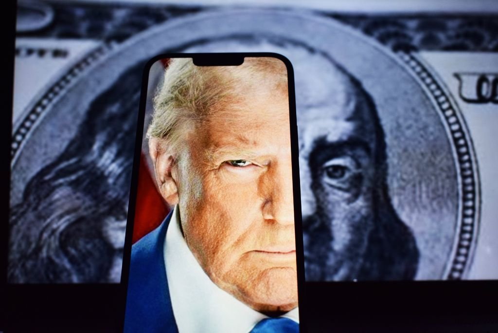 Close-up of a smartphone displaying a serious expression, framed by a background featuring a hundred-dollar bill, symbolizing wealth and power.