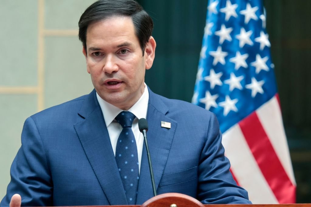 U.S. Senator Marco Rubio speaks at a podium with the American flag in the background, addressing key issues in a formal setting.
