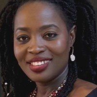 Portrait of a smiling woman with braided hair, wearing earrings and a necklace, against a dark background.