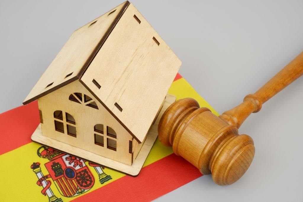 Wooden house model and gavel on a Spanish flag, symbolizing real estate law and property rights in Spain.