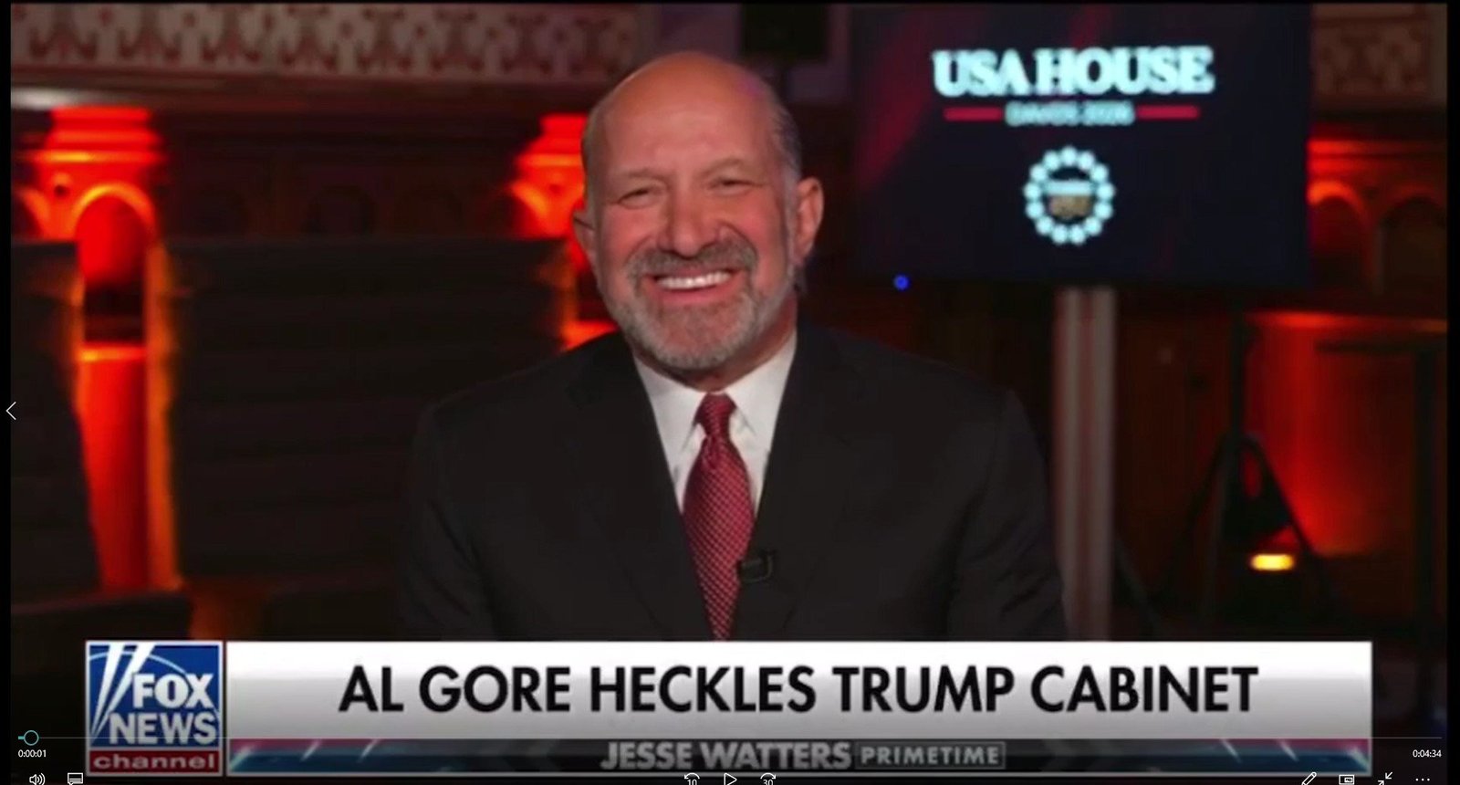 Smiling man in a suit discusses Al Gore's remarks about the Trump cabinet on a Fox News program, with a lit background and a USA House logo visible.