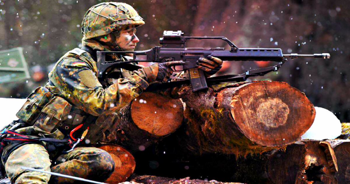 Soldier in camouflage gear aiming a rifle while taking cover behind logs in a snowy forest environment.