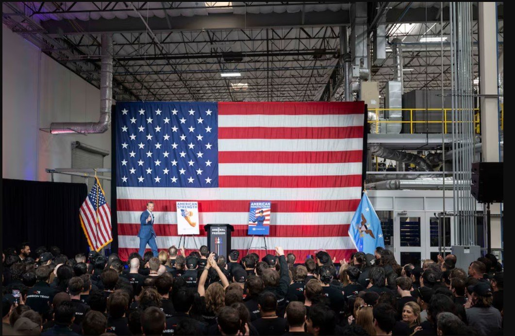 A speaker addresses an audience in front of an American flag backdrop at a corporate event, showcasing patriotism and community engagement.