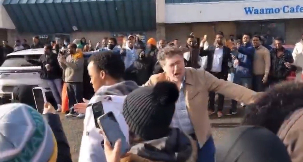 Crowd gathered outside Waamo Cafe, celebrating and capturing the moment on their phones, with a man animatedly engaging with the audience.