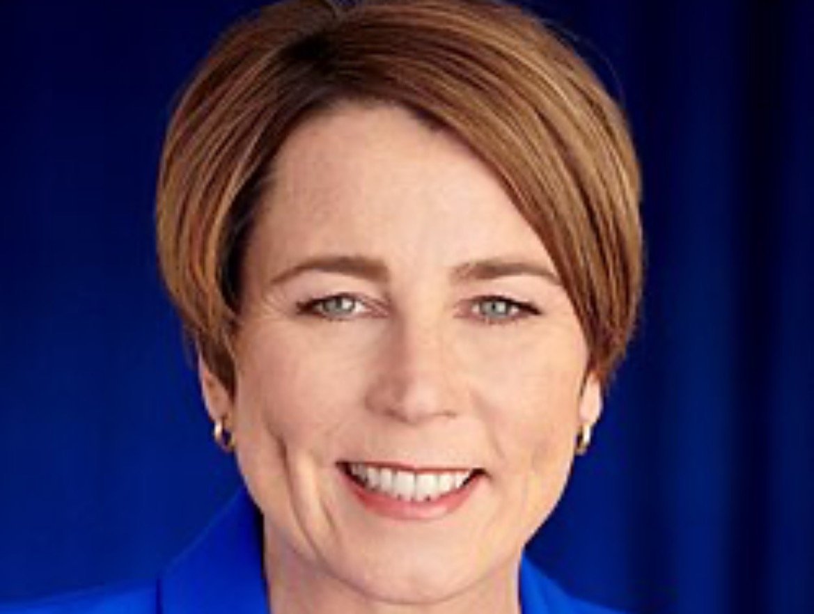 Professional headshot of a woman with short brown hair, smiling, wearing a blue blazer against a blue background.