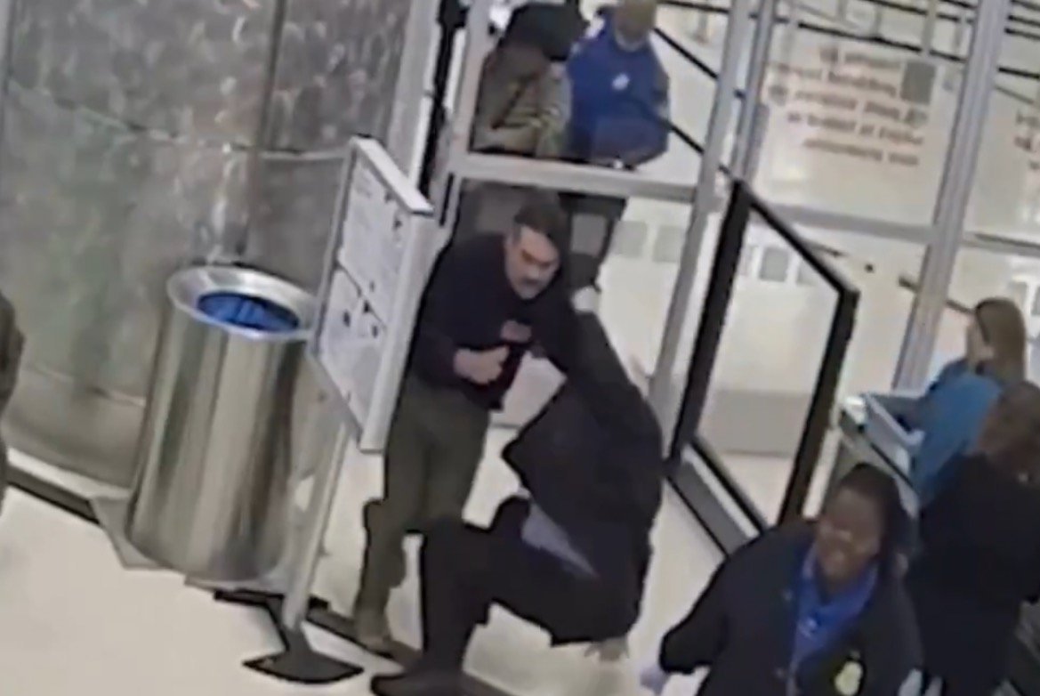 Security footage captures an altercation at an airport where a man is restrained by a security officer, with other personnel observing the situation.