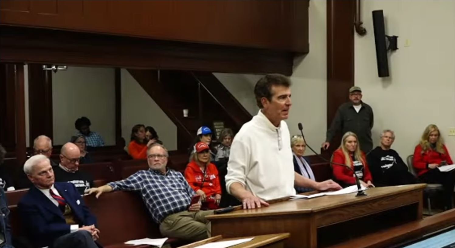 Public meeting with a speaker addressing an audience, focusing on community issues and civic engagement in a formal setting.