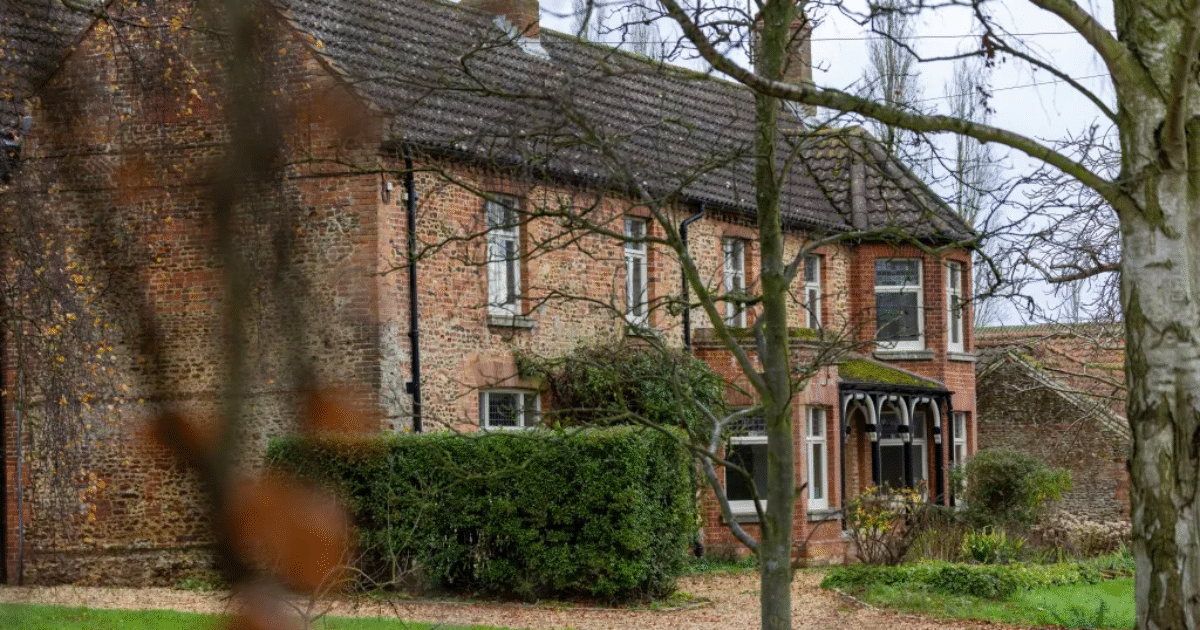 Historic brick house surrounded by lush greenery and trees, showcasing traditional architecture in a tranquil outdoor setting.