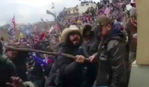 Crowd of protesters at a rally, with individuals engaging in a confrontation, flags visible in the background.