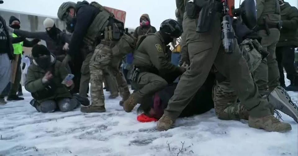 Law enforcement officers confront protesters in a snowy environment, highlighting tensions during a demonstration.