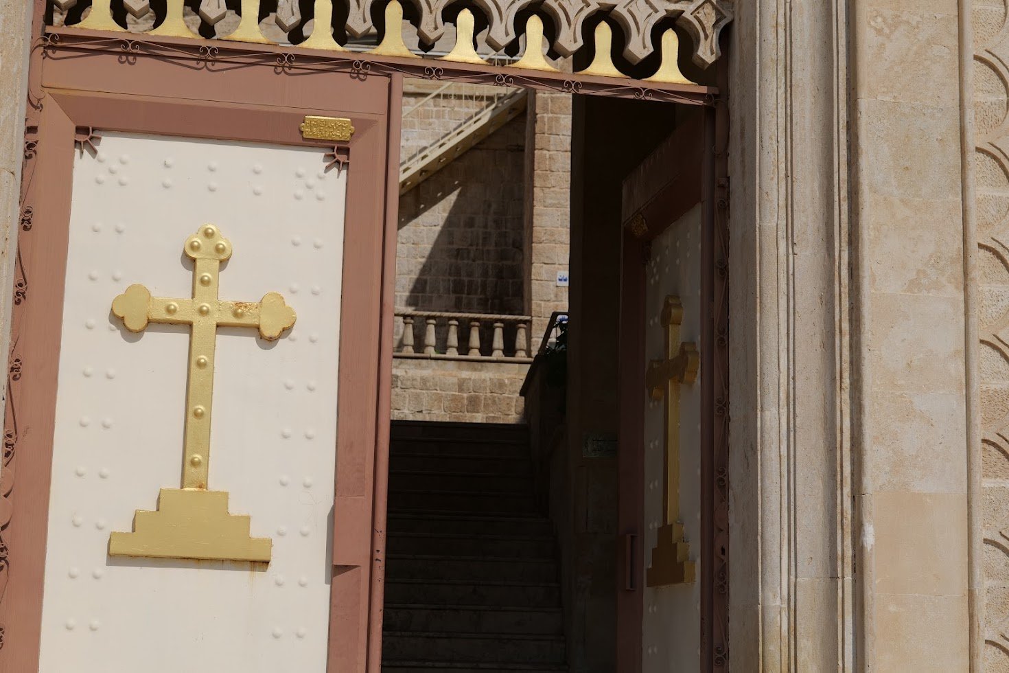 Golden cross adorns an ornate door leading to a stone staircase, showcasing architectural details and inviting entry.