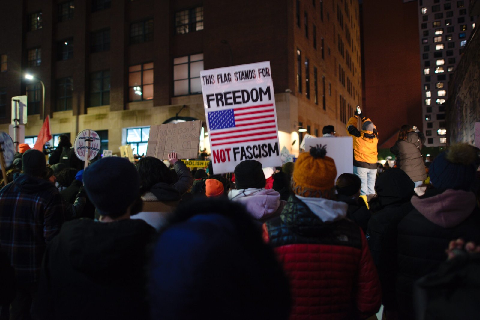 Crowd holding protest signs advocating for freedom and against fascism during a nighttime demonstration in an urban setting.
