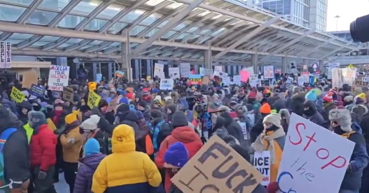 Crowd of protesters gathered outside a building, holding signs with various messages advocating for social justice and change during a winter demonstration.