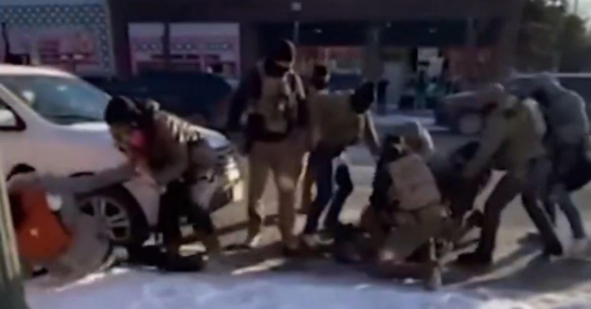 Law enforcement officers apprehending a suspect on a snowy street, with multiple individuals involved in the arrest.