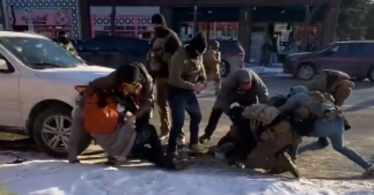 A group of individuals engaged in a physical altercation on a street, with nearby vehicles and storefronts visible in the background.