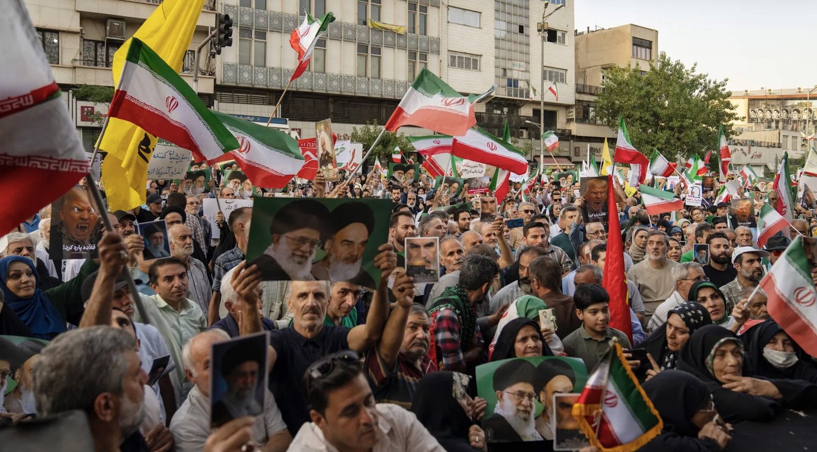 Crowd of protesters in Iran holding flags and signs during a demonstration, showcasing national pride and political sentiments.