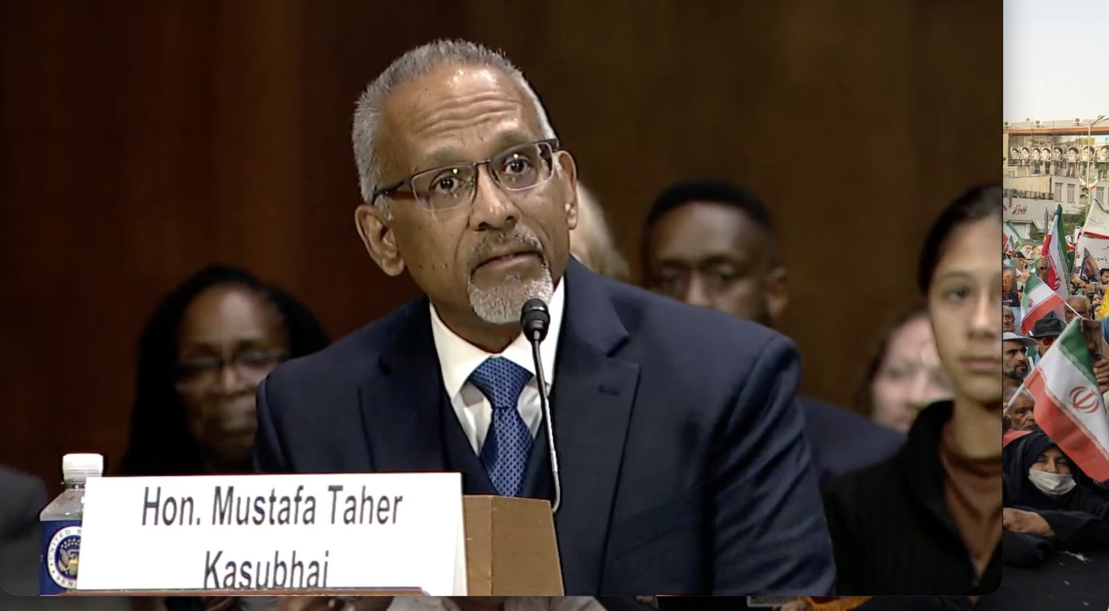 Hon. Mustafa Taher Kasubhai testifies during a Senate hearing, addressing key issues with an audience in the background.