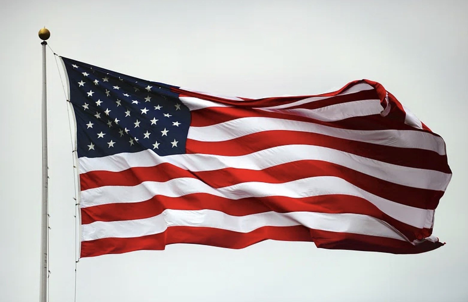 American flag waving against a gray sky, showcasing red and white stripes with blue field of stars, symbolizing patriotism and national pride.