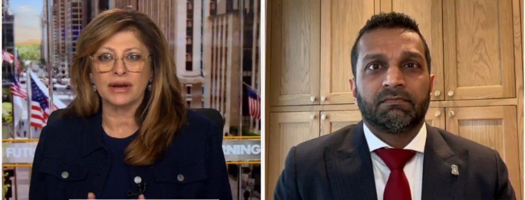 News interview featuring a female host and a male guest discussing current events, with a cityscape background and American flags visible.