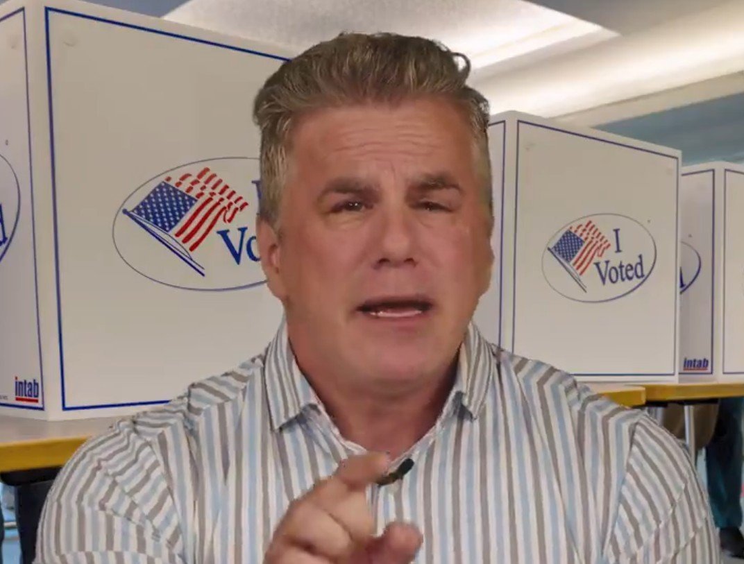 Man speaking passionately in front of voting booths with "I Voted" stickers, emphasizing the importance of civic engagement and participation in elections.