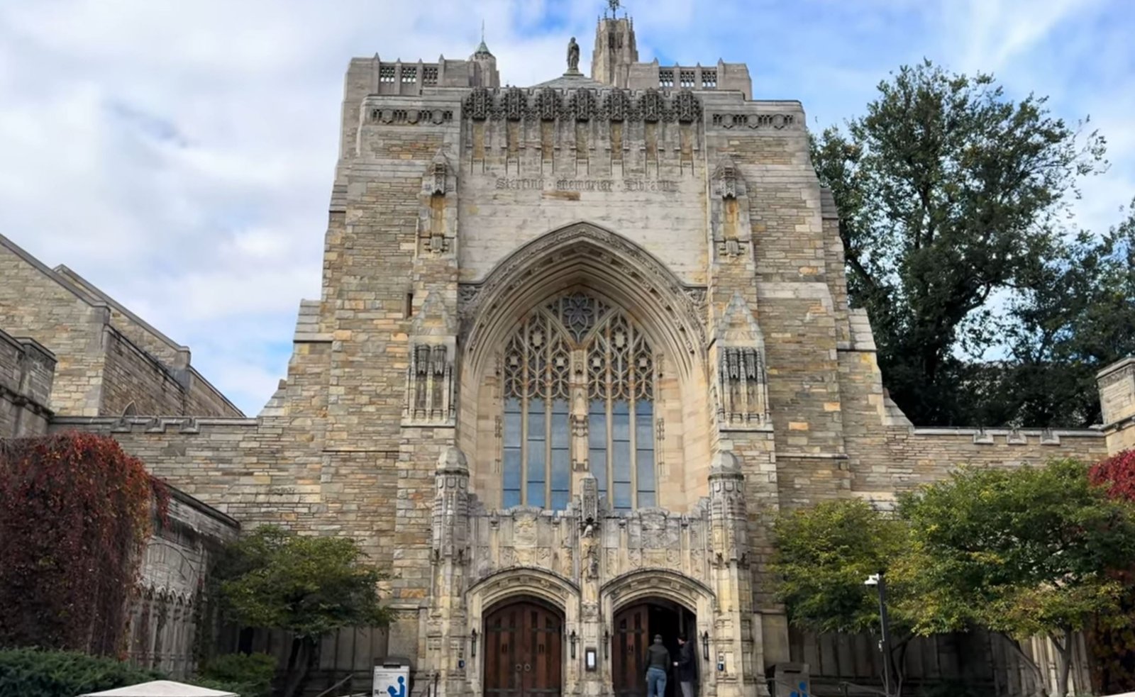Gothic-style architecture of Sterling Memorial Library at Yale University, featuring intricate stonework and large arched windows, surrounded by trees and greenery.