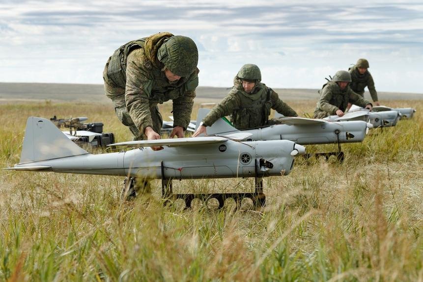 Soldiers preparing unmanned aerial vehicles (UAVs) for deployment in a grassy field, demonstrating military drone technology in action.