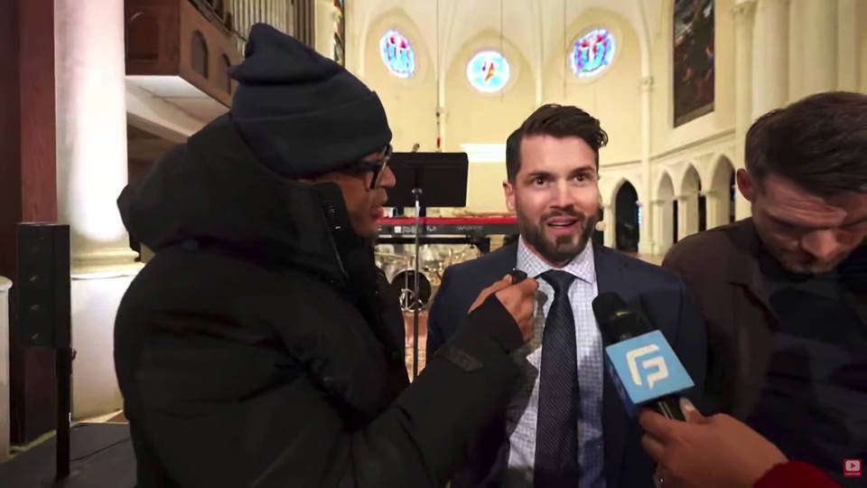 Two men engage in a conversation while being interviewed in a beautifully lit church setting, showcasing stained glass windows and musical instruments in the background.