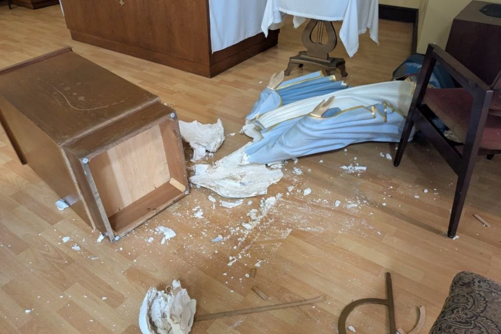 Damaged wooden cabinet and broken religious statue on the floor, highlighting a scene of disarray in a church interior.