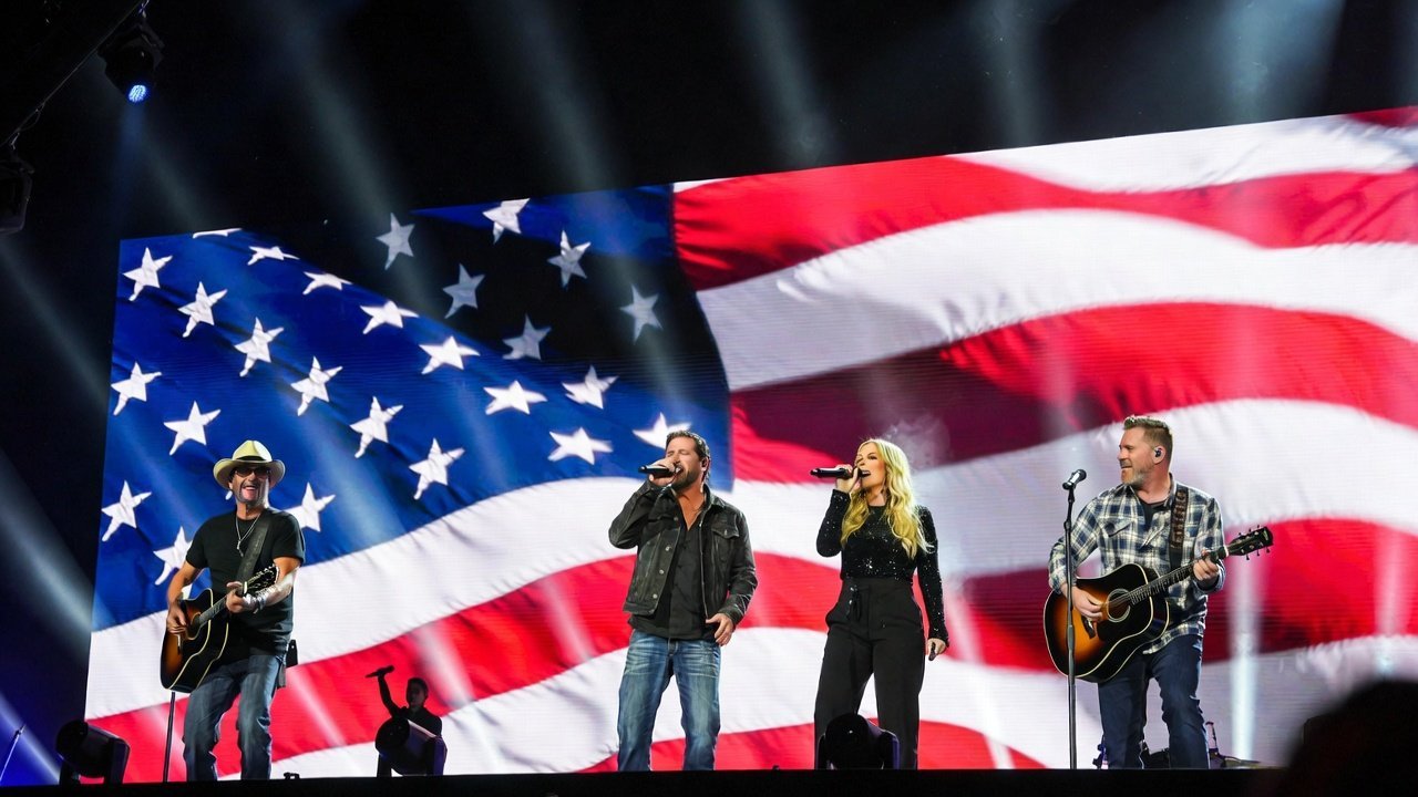 Country music artists perform on stage with a backdrop of the American flag, showcasing a vibrant live concert atmosphere.