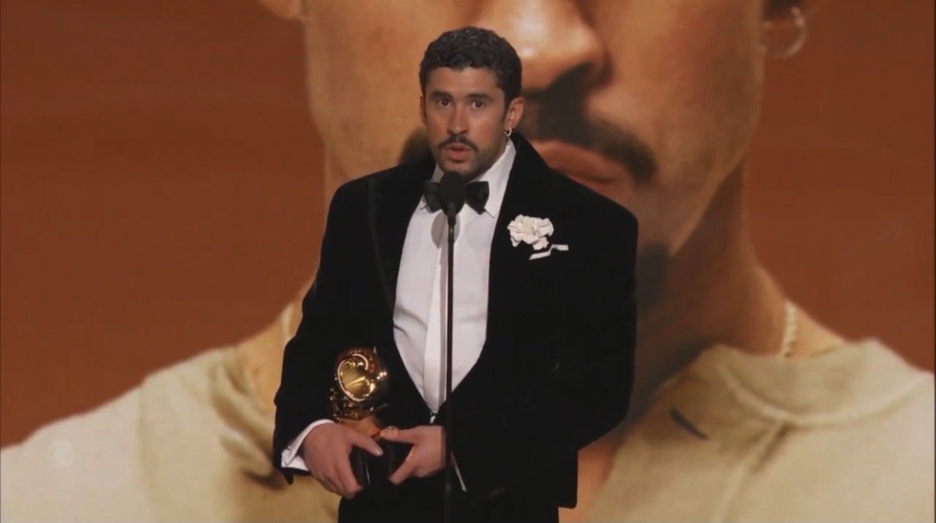 Award recipient delivering a speech at a prestigious ceremony, holding a trophy, with a large artistic backdrop.