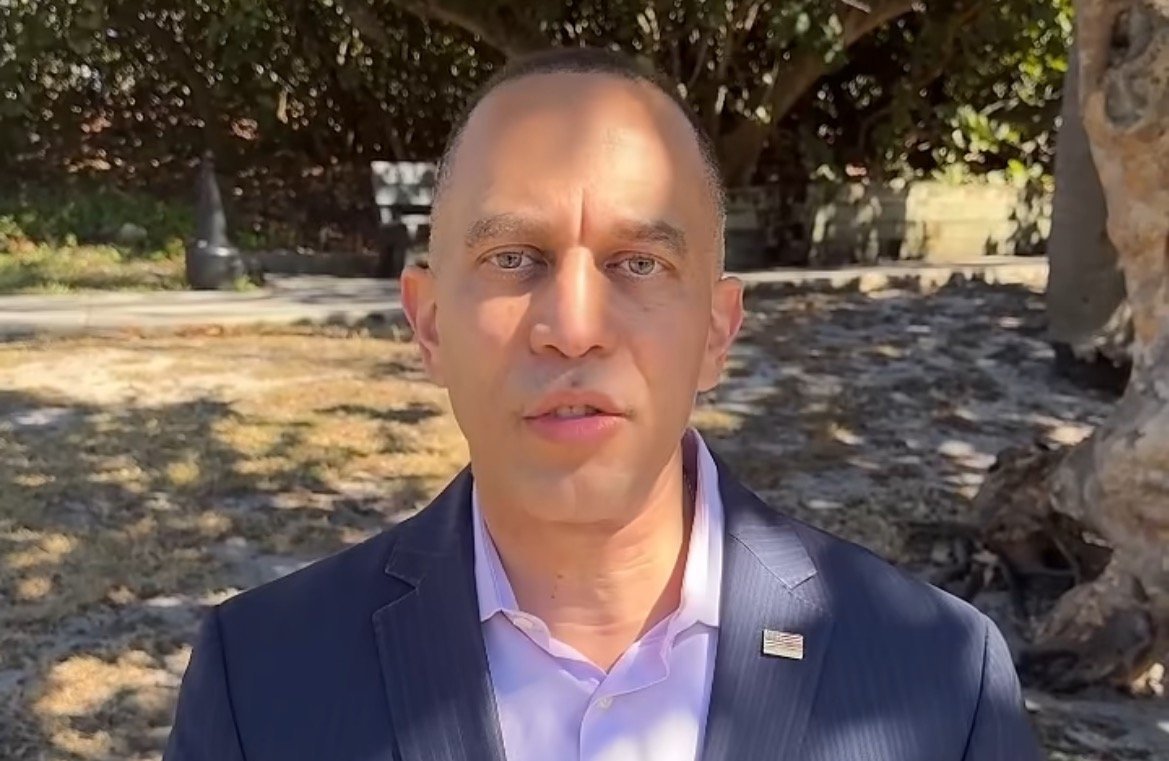 Man in a suit speaking outdoors, surrounded by trees and grass, conveying a professional message or announcement.