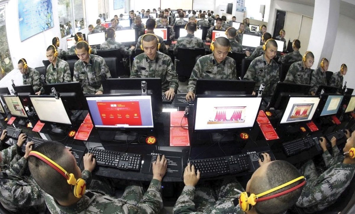 Military personnel engaged in computer training at a technology facility, wearing headsets and focused on their screens.