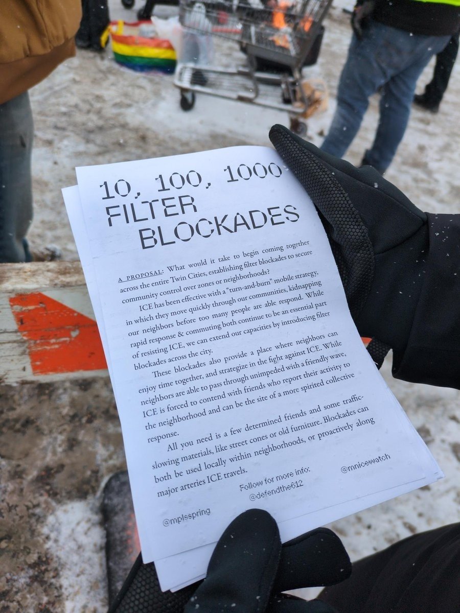 Hand holding a printed document about establishing filter blockades in the Twin Cities to enhance community safety and resist ICE activities, with a colorful background of flags and snow.