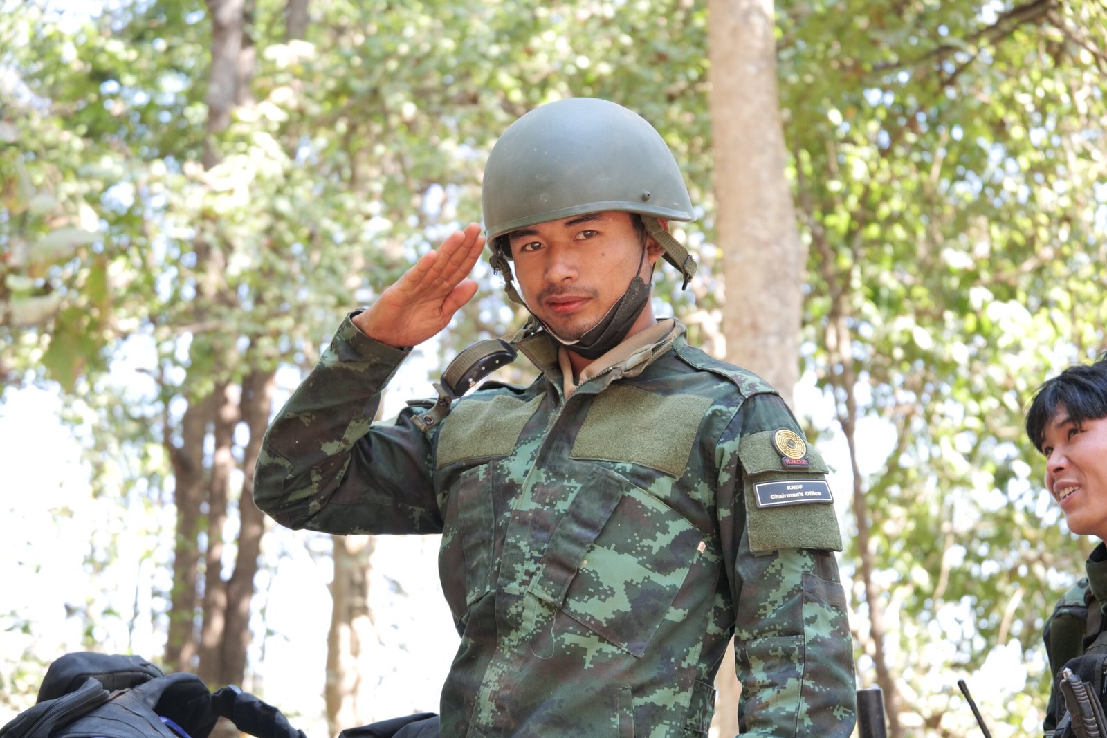Soldier in camouflage uniform saluting in a forested area, showcasing military pride and discipline.