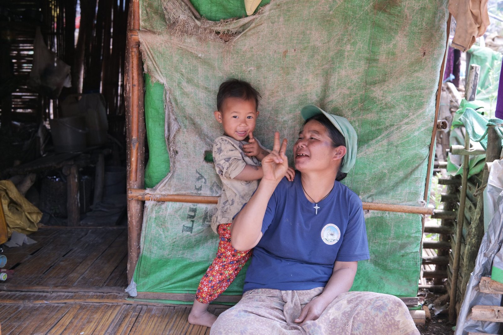 A joyful woman and child share a playful moment inside a rustic home made of bamboo and fabric.