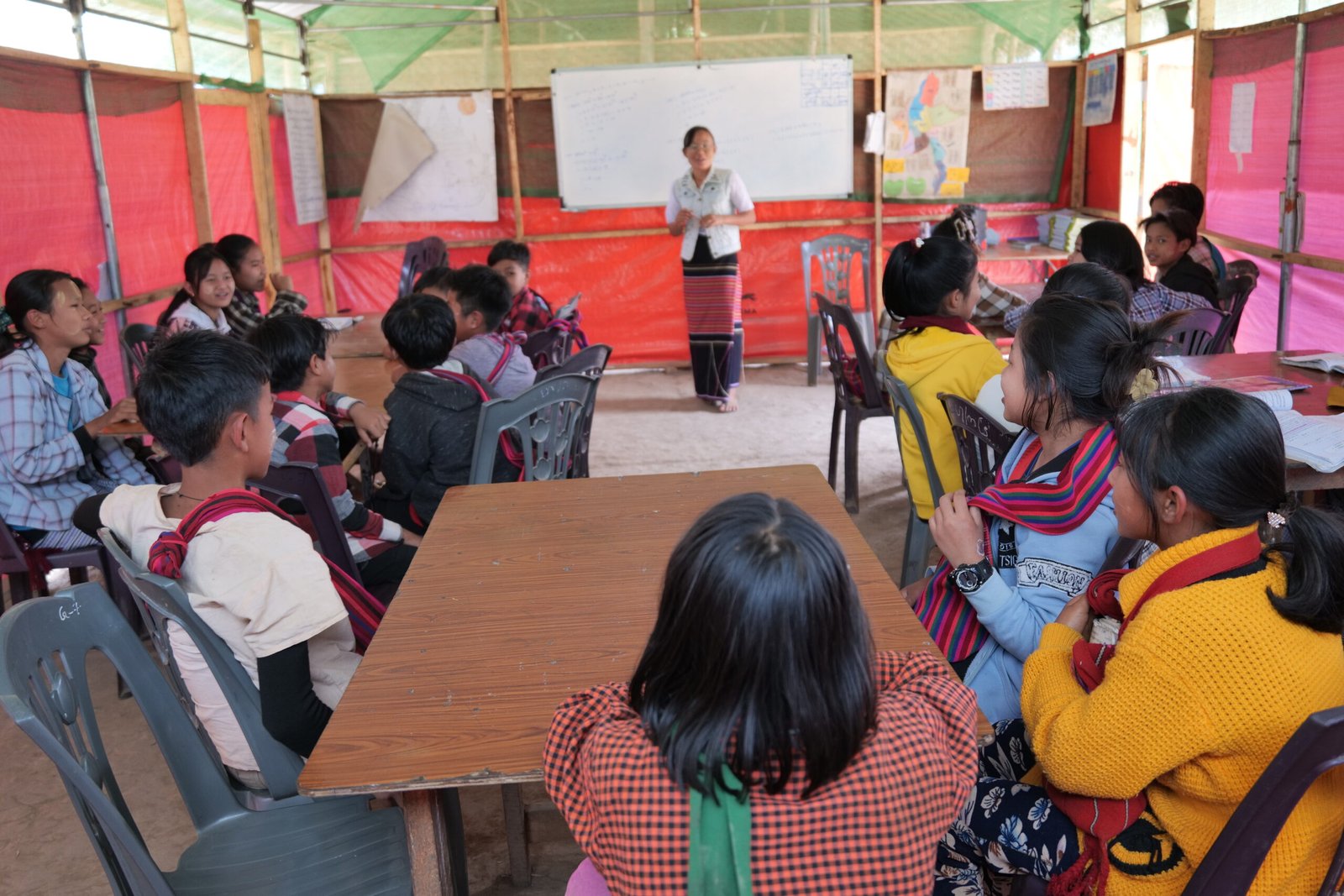 Students attentively listen to a teacher in a colorful classroom setting, highlighting an engaging educational environment for young learners.