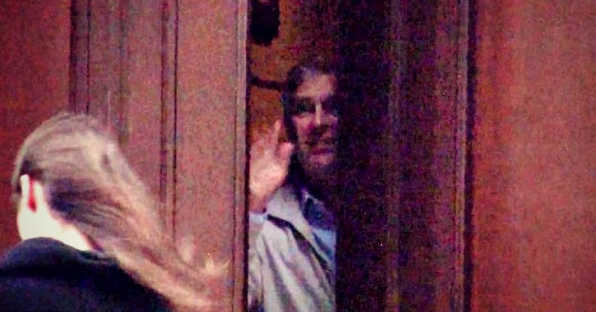 Person waving from behind a partially open door, with another figure walking away in the foreground.